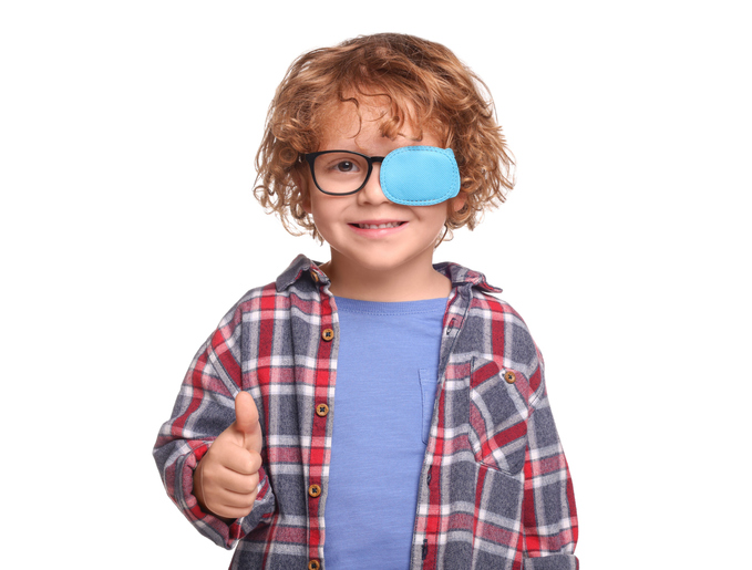 Happy boy with eye patch on glasses showing thumb up against white background. Strabismus treatment